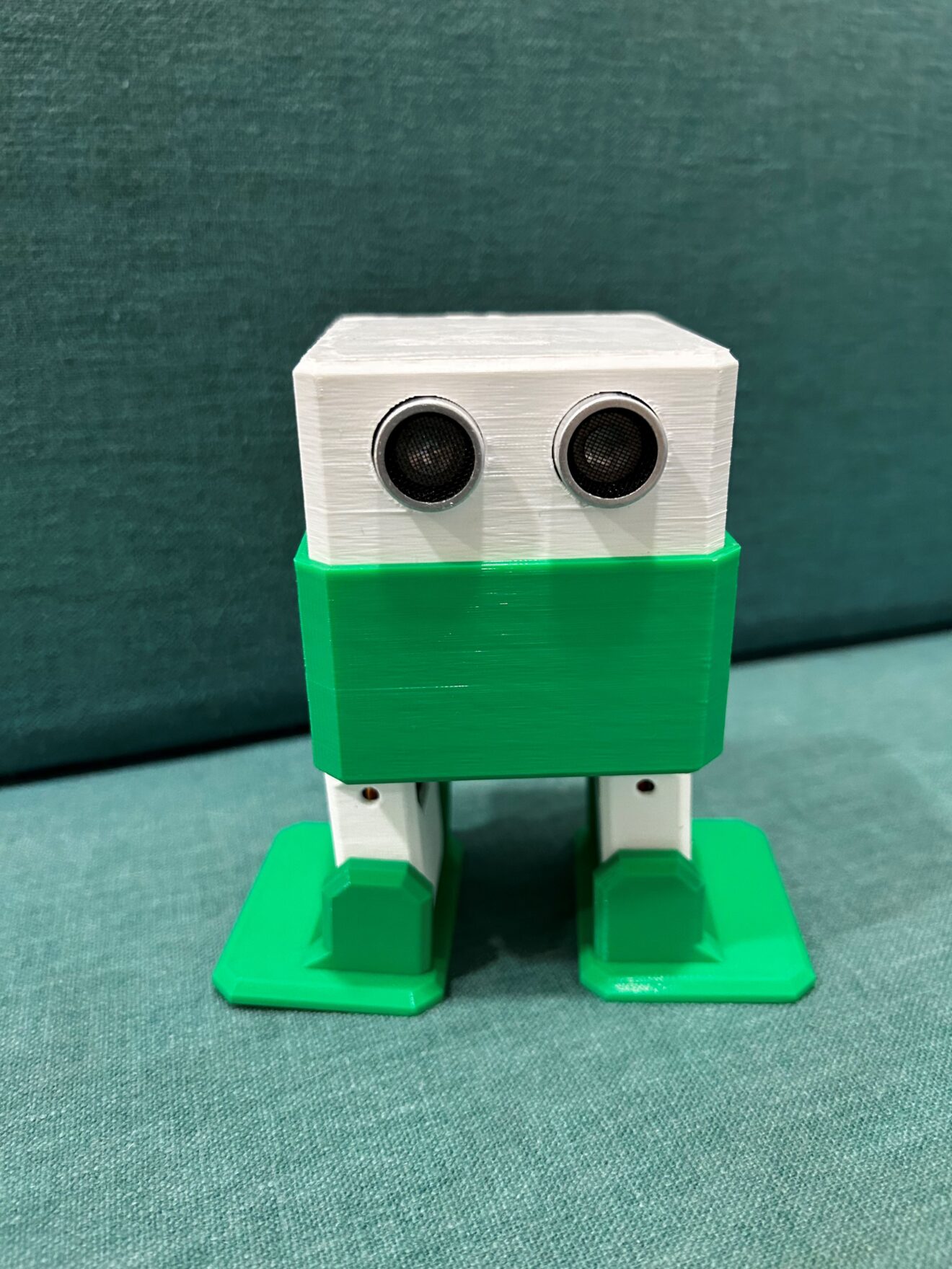 a green and white 3D printed robot with a boxy head and two feet.
